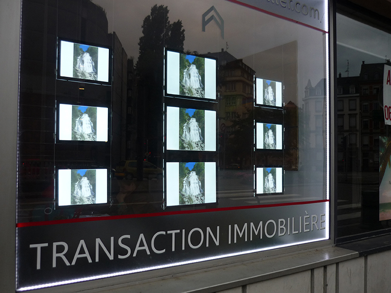 Impressions affichées sur écrans rétroéclairés dans la vitrine d'une agence immobilière
