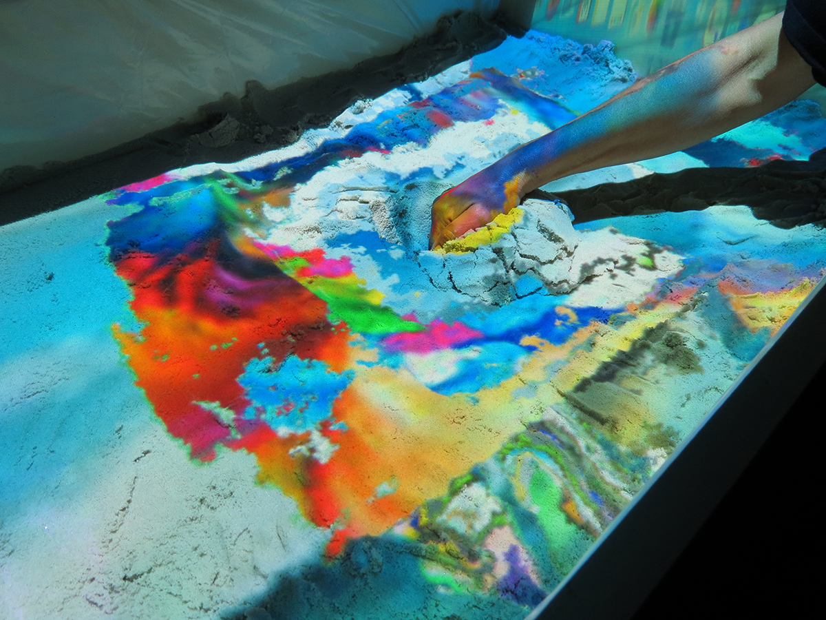 Photograph of the installation in use by a person digging into the sand to reveal layers of images