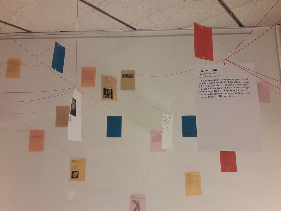 Photograph of the display window viewed from the outside, with the label “en français au pluriel(.fr)” affixed to the glass and the public strolling through the installation of texts