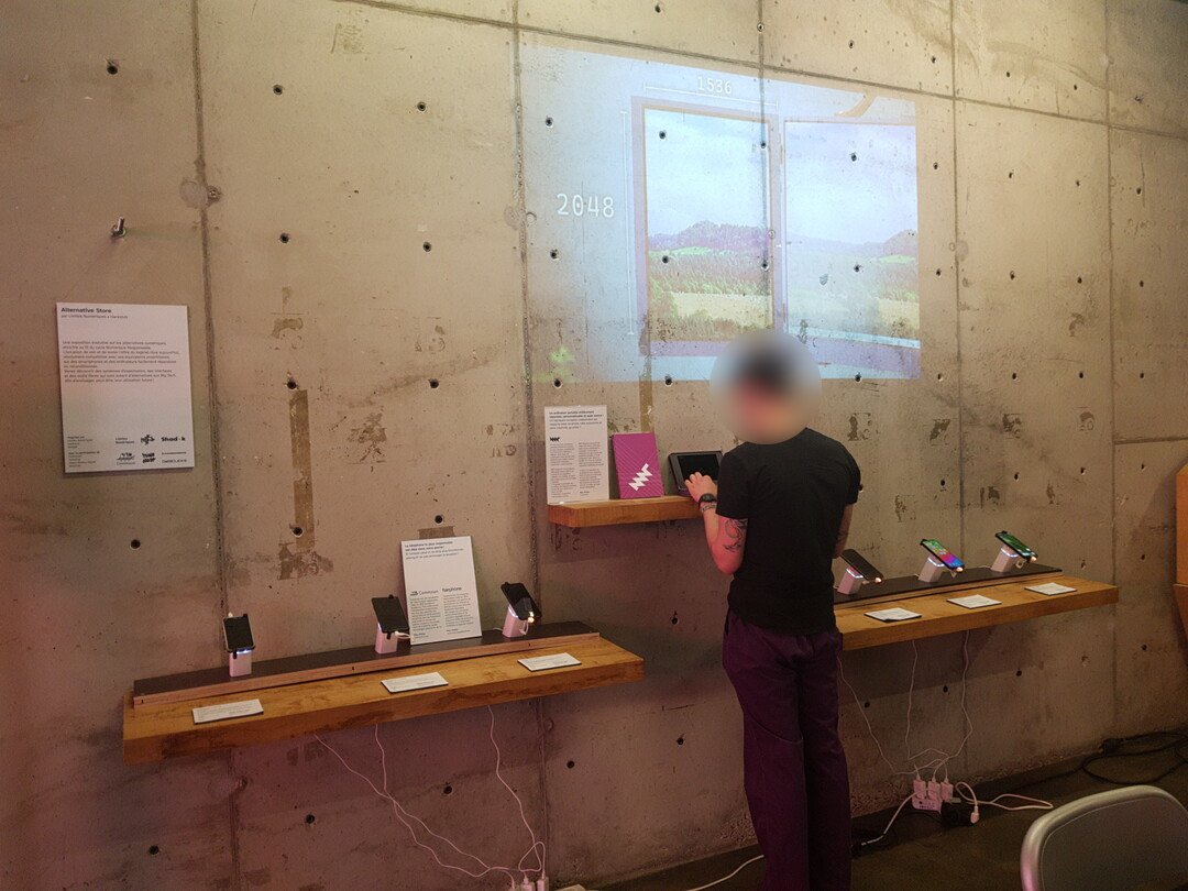 An overview of the Alternative Store exhibition, focusing on a projection, a series of 6 Fairphones and an MNT Pocket Reform