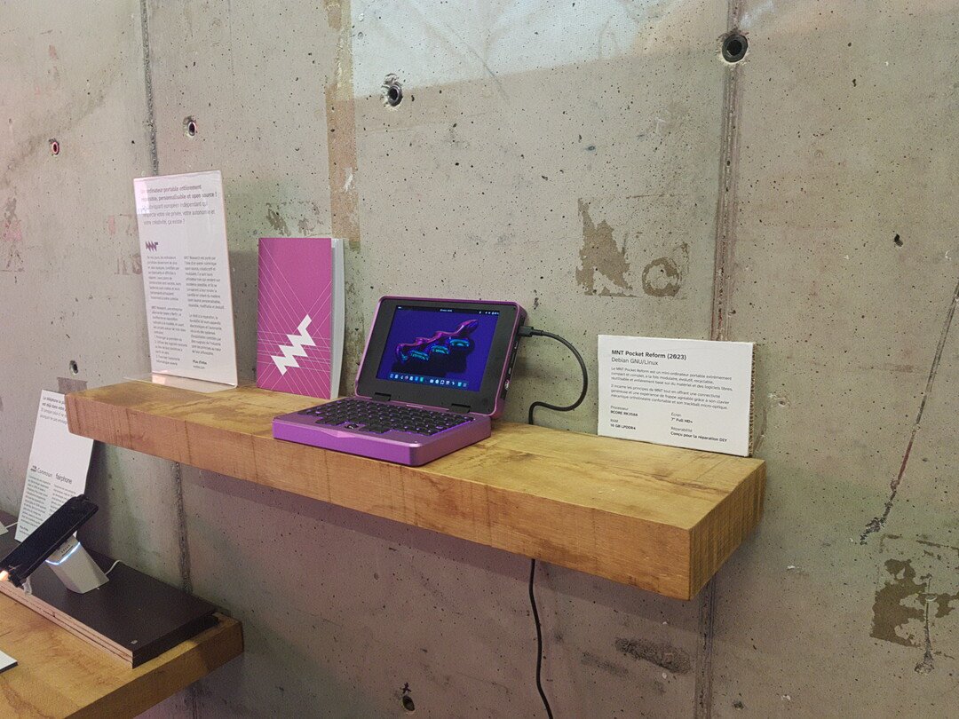 Close-up of the MNT Pocket Reform displayed on a shelf with labels and a user manual