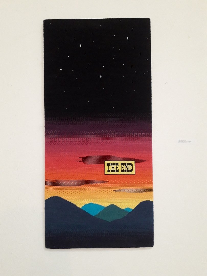 Tissage représentant un paysage de coucher de soleil sur une vallée surplombée d'un ciel étoilé avec la mention The end 